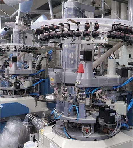 Industrial knitting machine used for manufacturing socks in a textile factory setting, featuring multiple spindles and automated components for efficient sock production.
